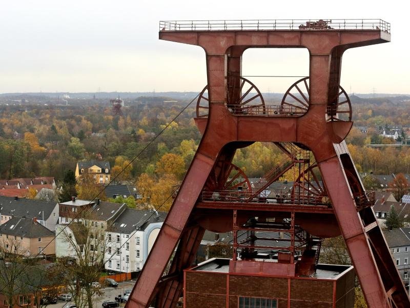 Hinter dem Förderturm der Zeche Zollverein in Essen haben sich die Baumkronen der Stadtbäume herbstlich gefärbt.