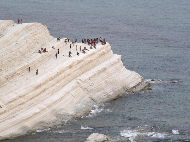 Menschen finden Komfort in der Meeresbrise auf der Scala dei Turchi, einer felsigen Klippe an der Küste von Realmonte im Süden Siziliens.