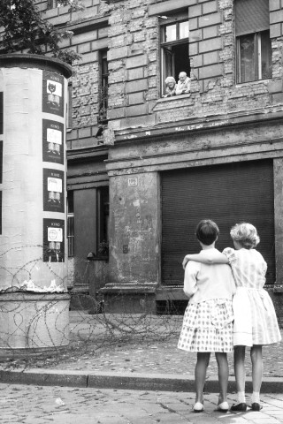 Am 14. August 1961 entstand diese Aufnahme: Zwei Kinder auf einer westdeutschen Straße unterhielten sich mit ihren Großeltern, die sich aus einem Fenster des genüberliegenden Hauses lehnten. Das Haus befand sich im östlichen Sektor. Ein Stacheldraht trennte die zwei Paare. 