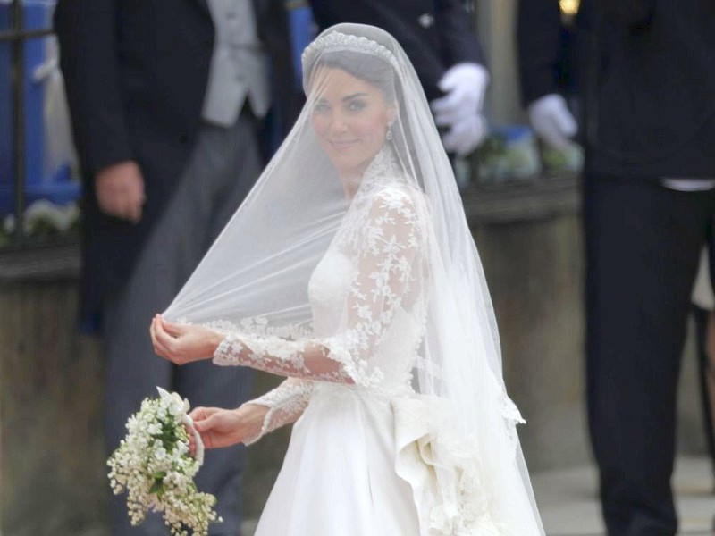 ...aus weißer Spitze wurde von Sarah Burton, Kreativdirektorin bei Alexander McQueen, entworfen. Die Haare trug die Braut offen, darin ein Diadem, drüber den Schleier. Die Hochzeit fand...