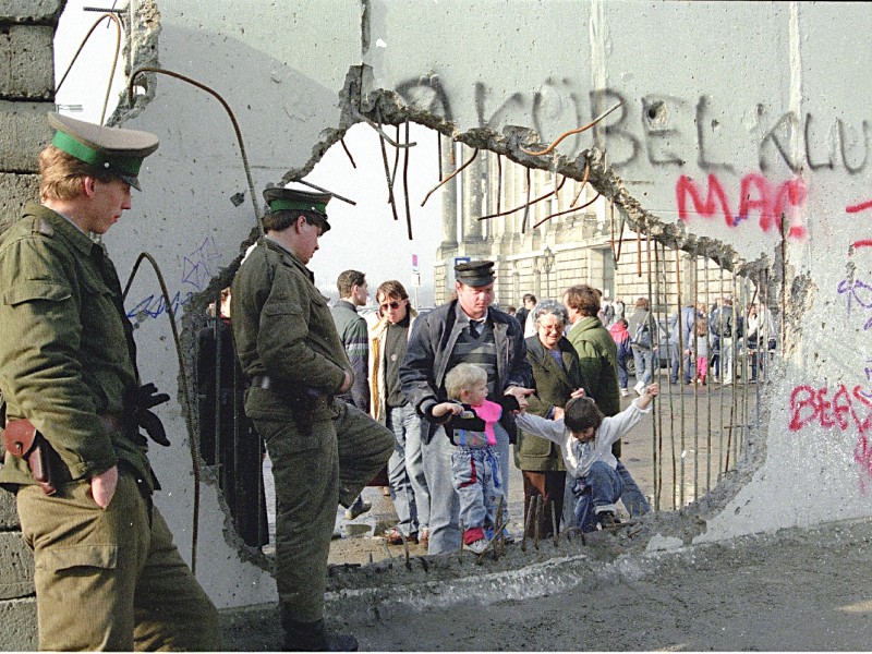 Der ehemals scharf bewachte Grenzstreifen war durch die Löcher der Mauerspechte zugänglich geworden. Wie hier direkt am Reichstag ließen die Grenzsoldaten auch Familien durch die sinnlos und löchrig gewordene Mauer in das vormals hermetisch abgeriegelte Sperrgebiet. Die Reste der inneren Armierung der Mauerelemente dienten nun als Haltegriffe für die kleinsten Besucher aus dem Westen. 