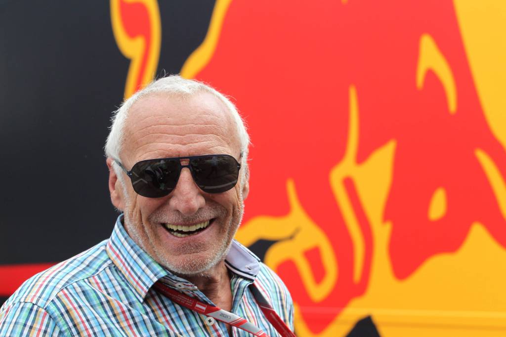 Dietrich Mateschitz lächelt vor dem Red-Bull-Logo in die Kamera.