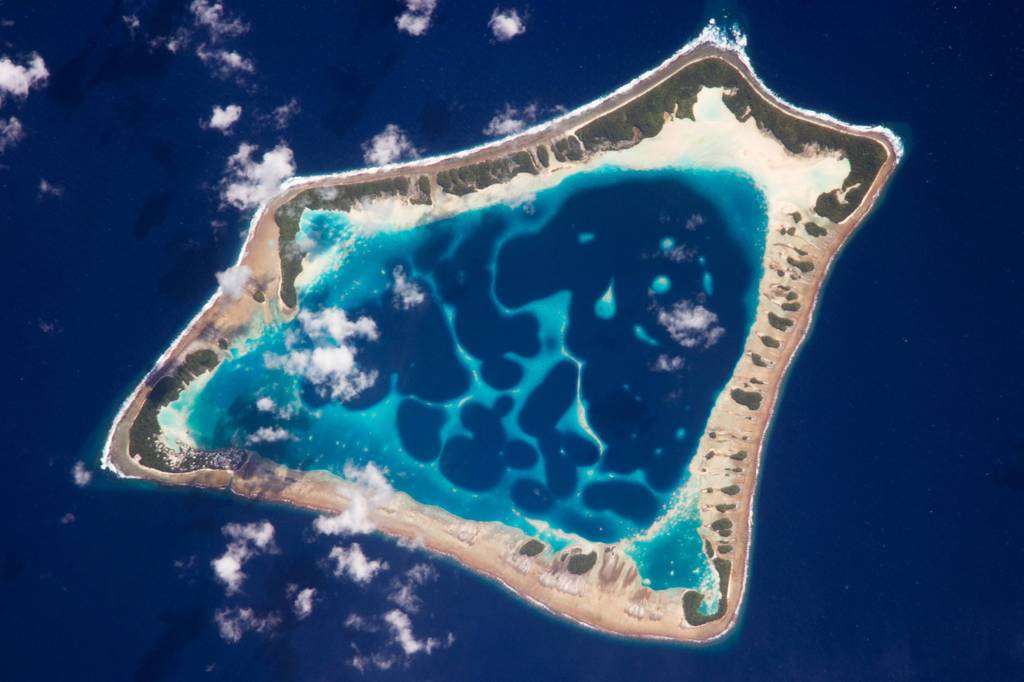 Eine Luftaufnahme von einem fünfeckigen Riff, das eine Lagune im Pazifik umschließt. Es ist das kleinste Atoll der Inselgruppe Tokelau.