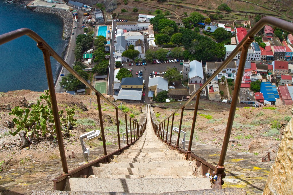 Ein steiler Blick in die Tiefe auf der Spitze einer steinigen Treppe zu einem bewohnten von Felswänden umgebenen Tal auf St. Helena im Südatlantik.