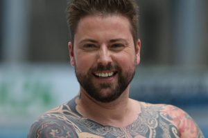 Schauspieler Felix von Jascheroff in einer horizontalen Portraitaufnahme. Er lächelt, hat braune hochgegelte Haare. Man sieht ebenfalls Tattoos auf seinem Oberkörper.