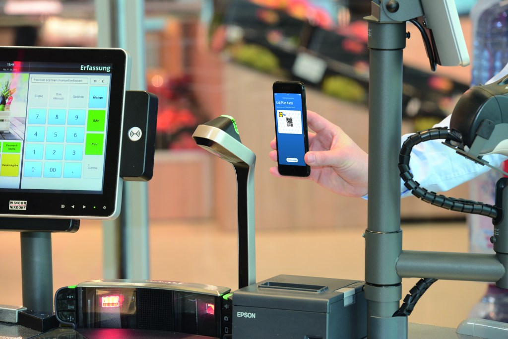 An einer Lidl Kasse hält ein Kunde sein Smartphone vor dem Scanner um Kontaktlos zu bezahlen.