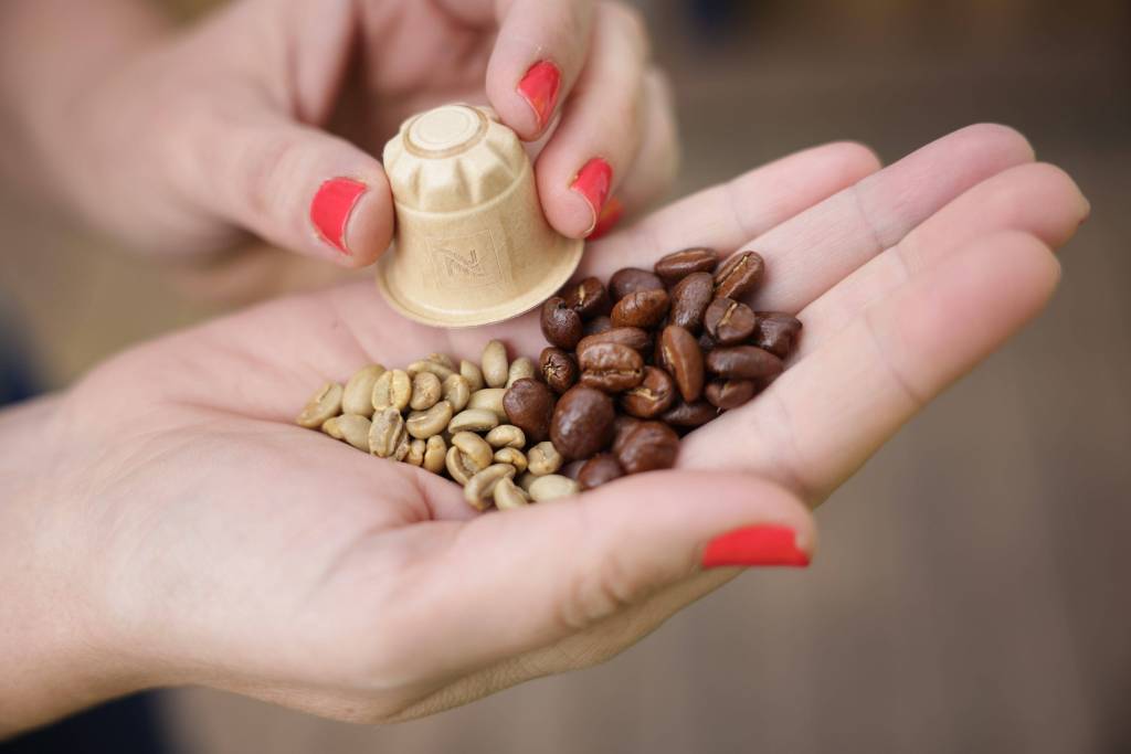 Kaffeebohnen und Kapsel auf Handfläche.