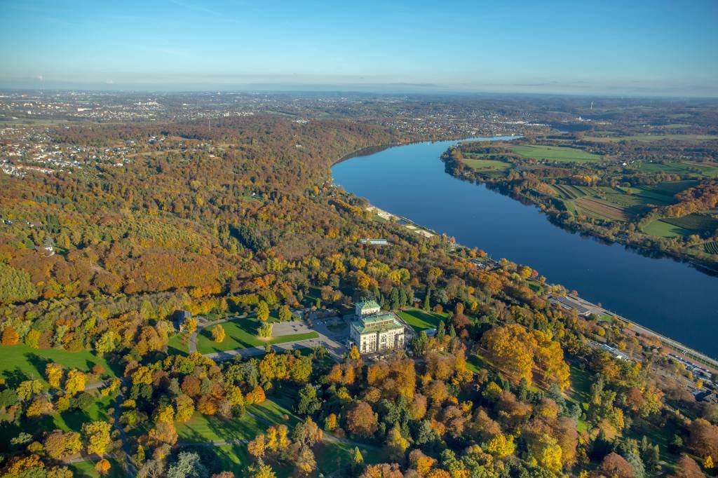 Der Baldeneysee in Essen umrahmt von Wald auf dessen Hügel die Villa Hügel thront. Der Baldeneysee ist eine der beliebtesten Essen Sehenswürdigkeiten, umgeben von grünen Hügeln und ein Paradies für Natur- und Wassersportliebhaber.