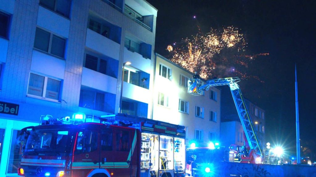 In Dortmund löschte die Feuerwehr einen Wohnungsbrand, ausgelöst durch eine Silvester-Rakete. Währenddessen erfüllt Feuerwerk den Himmel über der Stadt.