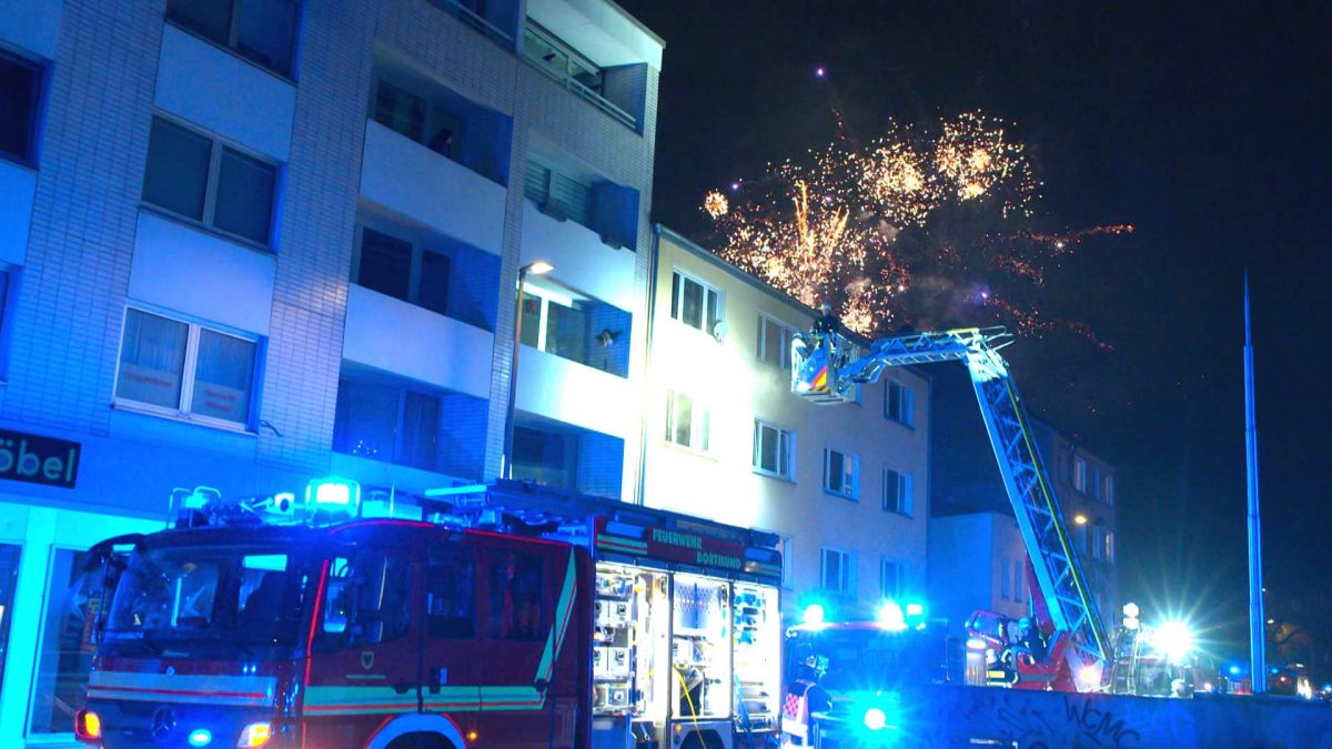 In Dortmund löschte die Feuerwehr einen Wohnungsbrand, ausgelöst durch eine Silvester-Rakete. Währenddessen erfüllt Feuerwerk den Himmel über der Stadt.