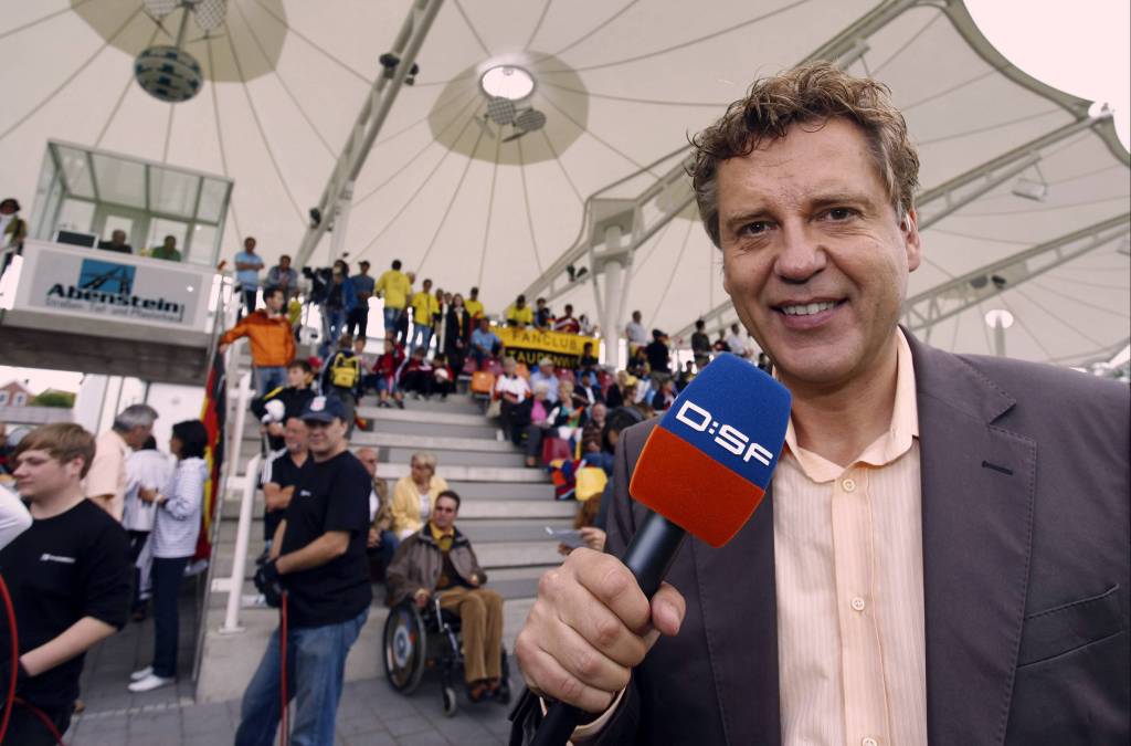 Jörg Dahlmann mit Mikrofon vor Tribüne im Stadion.