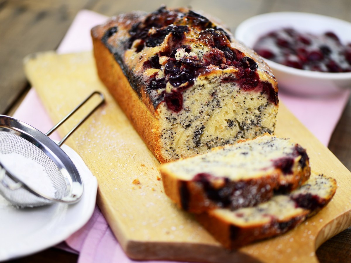 Angeschnittener Mohnkuchen mit Kirschen auf einem Holzbrett